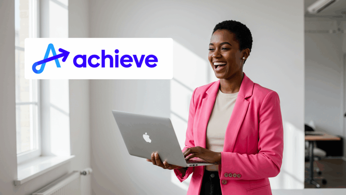 A cheerful woman in a bright pink blazer holding a laptop and laughing in a sunlit office, with the Achieve logo overlaid on the left side.