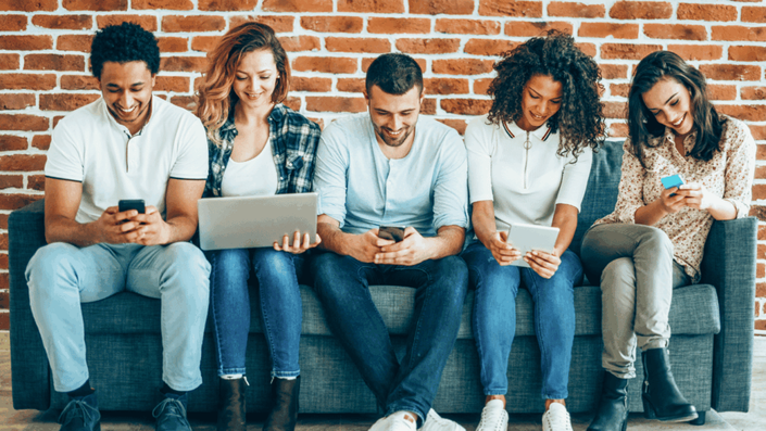 A diverse group of people collaboratively using a laptop, tablet, and smartphone with financial charts on screen, representing the broad appeal of Digital Banking across different users.
