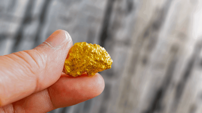 Hand carefully holding a raw gold nugget, illustrating the tangible and timeless appeal of Investing in Gold.