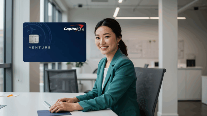 Smiling woman in a teal suit sitting at a clean, bright office desk with a Capital One Venture credit card graphic — promoting the Venture card as an ideal choice for business and travel perks.